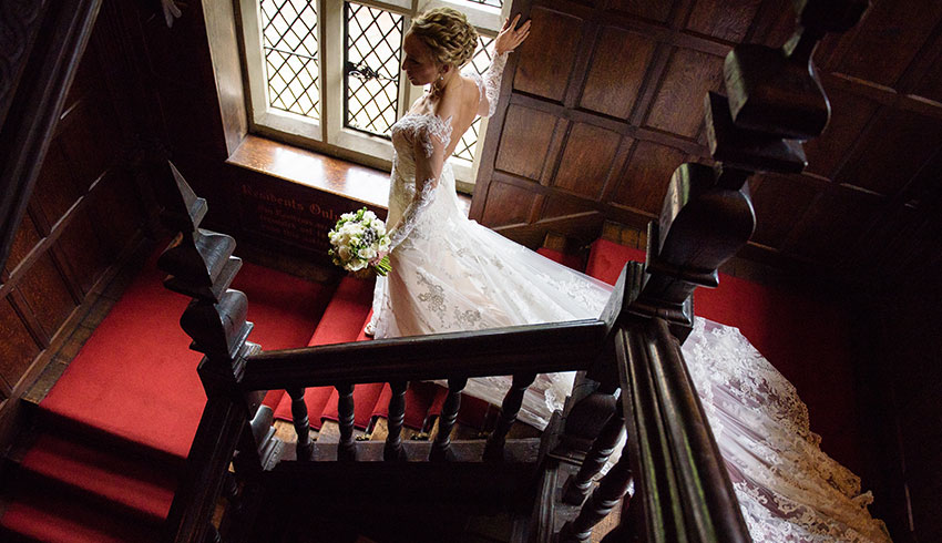 Bride coming down the sweeping staircase at Great Fosters, a Surrey wedding venue