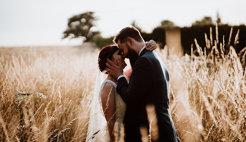 Wedding couple in a field surrounded by tall grass, image by Nicola Dawson Photography